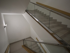 бетонные ступени лестничных маршей с перилами на освещенной лестничной клетке с белыми стенами подземного паркинга