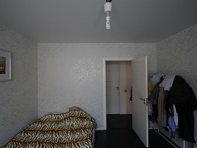 большая кровать с тигровым покрывалом, одежда на напольной вешалке за открытой дверью в спальную комнату просторной современной квартиры в Котельниках