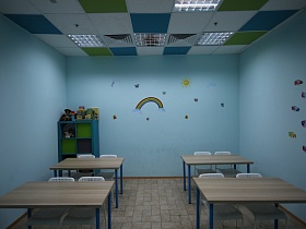ровные бежевые парты, белые стулья, синий шкаф с зелеными дверцами у голубых стен классной комнаты с разноцветными плитами на белом потолке учебной комнаты детского сада