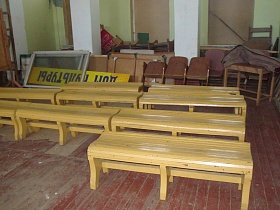 новые деревянные скамейки, запасные секционные кресла, желтая вывеска, оконные рамы, длинная деревянная лестница на старом окрашенном полу светлой комнаты с зашитыми окнами старого клуба СССР