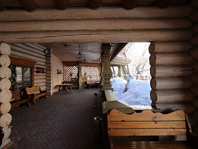 деревянные скамейки, круглый стол, металлические урны для мусора на открытой террасе с деревянными резными колонами под крышей ресторана из бревен в стиле сруба