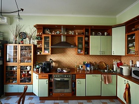 разнообразная посуда на полках закрытого шкафа, открытых полках мебельной стенки, электроприборы на столешнице коричневой кухни с салатовыми дверцами шкафчиков