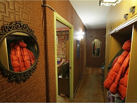 круглое зеркало в резной рамке на стене с коричневым пенопленом, мебельная стенка с одеждой на крючках в прихожей квартиры панельного дома СССР 80-89 гг стиля