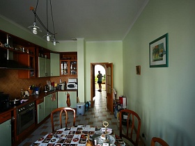 картины на салатовых стенах кухни с коричневой мебельной стенкой и круглым обеденным столом на плиточном полу большой стандартной семейной квартиры