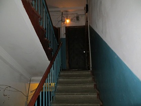 голубые панели на белых стенах подъезда с лестничными маршами и входными дверьми в квартиры на лестничной площадке жилого дома
