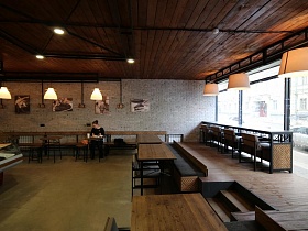 картины на светлых стенах с серой плиткой просторного стильного уличного кафе-кулинария с большими окнами и стеклянной витриной
