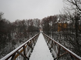металлическое ограждение с перилами на заснеженном длинном пешеходном подвесном мосту над протекающей рекой