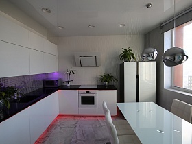 белая кухня с черной столешницей,белая вытяжка над встроенной газовой плитой, черный с белыми дверцами холодильник у стен серого цвета лаконичной квартиры в стиле хай-тек