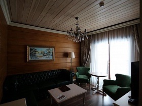 бежевый журнальный столик и черный мягкий диван у стены с картиной в деревянном съемном коттедже