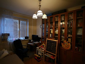 белый детский столик со стульчиком и доска для занятий у длинного книжного шкафа в гостиной двушки