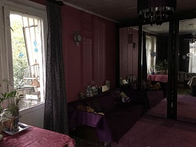 раскладной диван под фиолетовым покрывалом у стены с барометром между балконной дверью и большим черным шкафом-купе с зеркальными дверьми в сиреневой гостиной квартиры в Останкино