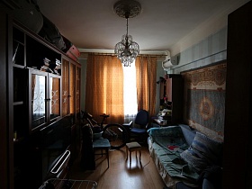 велосипед, табурет, черный компьютерный стул у окна с коричневыми шторами в комнате с голубыми обоями и голубой мягкой мебелью сталинской квыартиры