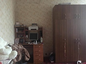 коричневый трехдверный шкаф для одежды с антресолью, монитор, колонки, принтер на компьютерном столе с полками в светлой спальной комнате квартиры СССР