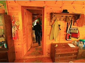 картина над шкафом с книгами, фартук на крючке, навесная полка с вещами и аккордеоном над комодом у входной двери в гостиную деревянной дачи музыканта