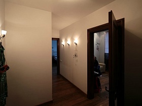 коричневые межкомнатные двери в спальную комнату и на кухню из просторной прихожей с бра на розовых стенах квартиры на 12 этаже