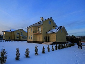 кирпичные двухэтажные дома с открытым балконом и крыльцом на входе на просторном участке с зелеными елочками в зимнее время