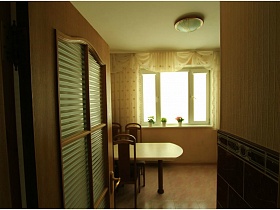 открытая дверь в светлую современную кухню с бежевым столиком и стульями со спинкой в трехкомнатной квартире