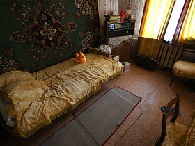 диван-раскладушка с желтым покрывалом у стены с зеленым ковром и ковриком на полу в гостиной дачи