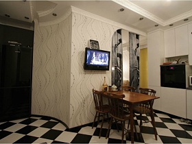 квадратные часы и плоский телевизор на белой стене с черными разводами в кухне квартиры с выходом на крышу магазина