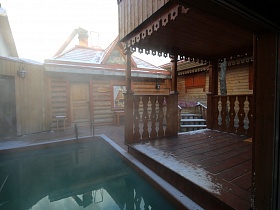 выход к бассейну с открытой деревянной веранды бревенчатого дома на территории банного комплекса