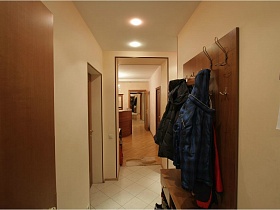 одежда на крючках коричневой мебельной стенки в светлой прихожей съемной трехкомнатной квартиры с ресепшн