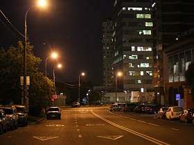 легковые автомобили на парковочных местах на широкой улице Крылатские холмы с ярким освещением фонарных столбов в ночное время