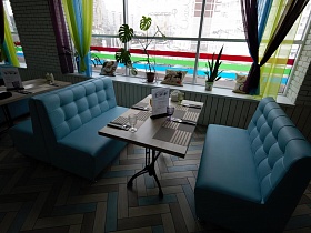 сервированный столик на ножках в индивидуальной зоне с мягкими голубыми диванчиками у большого окна с разноцветными шторами  Лофт Бара в спальном районе