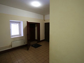 светильник на белом потолке чистого ухоженного светлого холла  с квадратной плиткой на полу с квартирами на этаже кирпичного дома