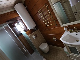 душевая кабина и нагревательный бак в углу ванной комнаты с деревянными стенами и потолком съемного коттеджа