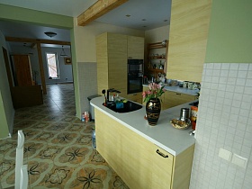 бежевый деревянный шкаф, деревянные полочки в углу красивой кухни с мозаичной плиткой панелей на стене элитного недостроенного дома