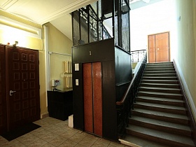 коричневые двери лифтовой кабины на первом этаже у лестничных маршей парадного подъезда СССР 2 со столиком вахтера
