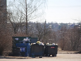 зеленая будка и заполненные мусорные контейнеры на отдельной площадке у дороги в городке Сычево