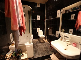 белая раковина с зеркалом, санузел,душевая кабина в ванной комнате с черной плиткой разнопланновой трехкомнатной квартиры