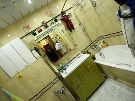 шкафчики, зеркало над раковиной с тумбой и белая ванна в ванной комнате салатового цвета большой квартиры врача
