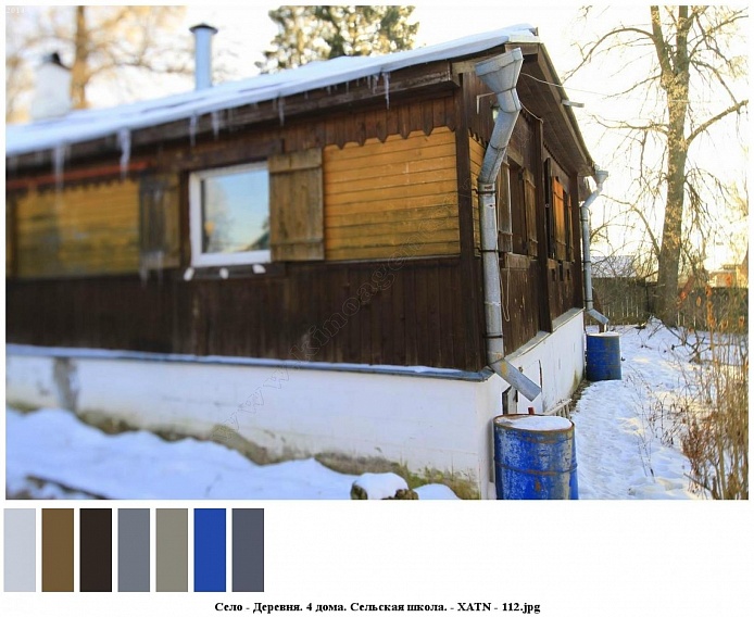 синие круглые железные боки под водосточными трубами на углах деревянного коричневого с желтым дома со ставнями на окнах на участке в снегу