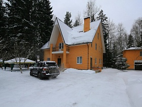 снег на треуголной крыше добротного кирпичного дома с балконом, крыльцом и колоннами на участке с машинами на снегу