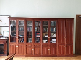 белый гипсовый бюст на поверхности коричневого деревянного декоративного камина у окна, длинный многодверный книжный шкаф и шкаф для одежды у стены светлого строгого кабинета КГБ СССР для съемок кино