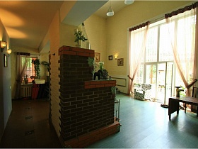 камин, обшитый кирпичем в центре просторной гостиной с панорамными окнами в доме под съем