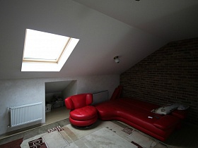 кожанный красный разложенный диван и кресло у стены, выложенной кирпичом в комнате отдыха с прямоугольным окном в крыше дома для съемок кино