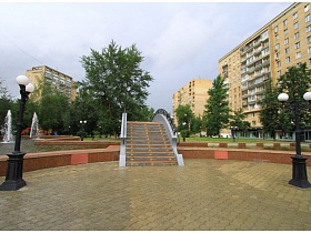площадь с фонарями на черных столбах перед фигурной лестницей моста в парке с фонтанами в жилом квартале
