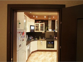 молочная мебельная стенка на кухне с бежевым линолеумом на полу и натяжным потолком через открытую дверь просторной современной простой квартиры с детской