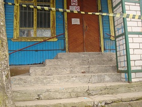 полосатая лента, перекрывающая вход на крыльцо с разбитыми ступенями у входных дверей старой деревянной больницы