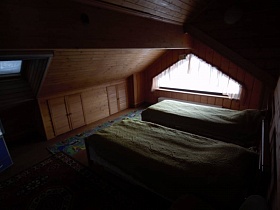 у треугольного окна две кровати с зелеными покрывалами