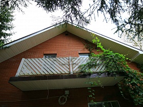длинный балкон на втором этаже под крышей семейного простого дома среди густого хвойного леса