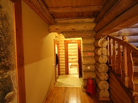 открытые двери в санкомнаты из светлого длинного коридора деревянного дома банного комплекса