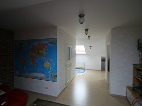 синяя карта мира на белой стене, круглые светильники на потолке комнат без дверей в мансарде жилого дома с яркой кухней