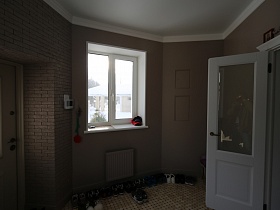 множество пар обуви на полу с мозаичной плиткой  вдоль стены с окном в прихожей современного двухэтажного коттеджа
