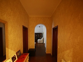 желтая прихожая с зеркалом на стене, дверьми в комнаты и арочным дверным проемом в гостиную современного кирпичного дома