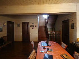 ноутбук и планшет на столе с ораньжевой скатертью в гостиной напротив деревянной лестницы современного трехэтажного дома