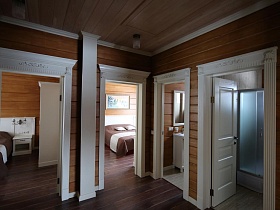 деревянный потолок, стены и пол в просторном холле съемного коттеджа с белыми рельефными лутками дверей